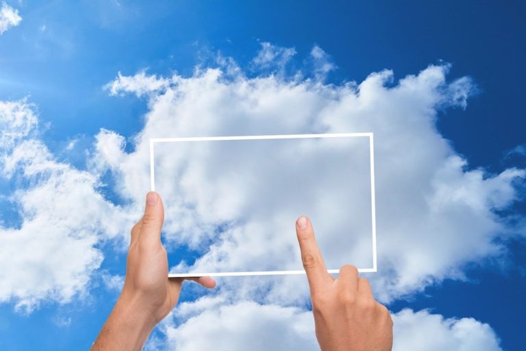 Hands holding an outline of a tablet superimposed over clouds in the sky