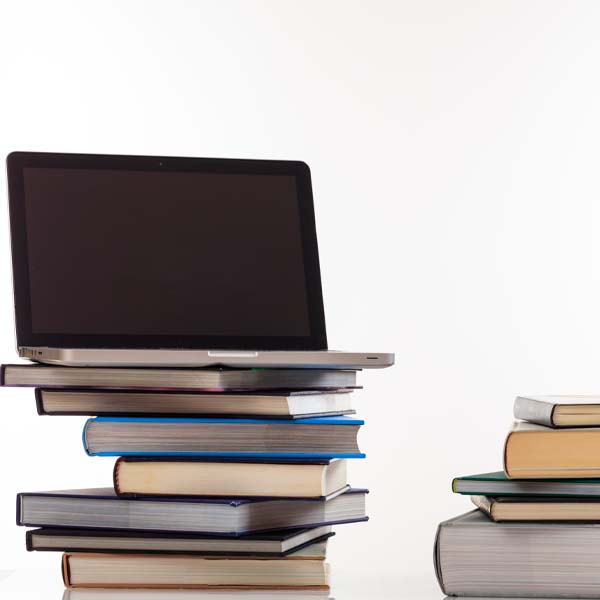 Laptop on top of a stack of books with more books to the right.